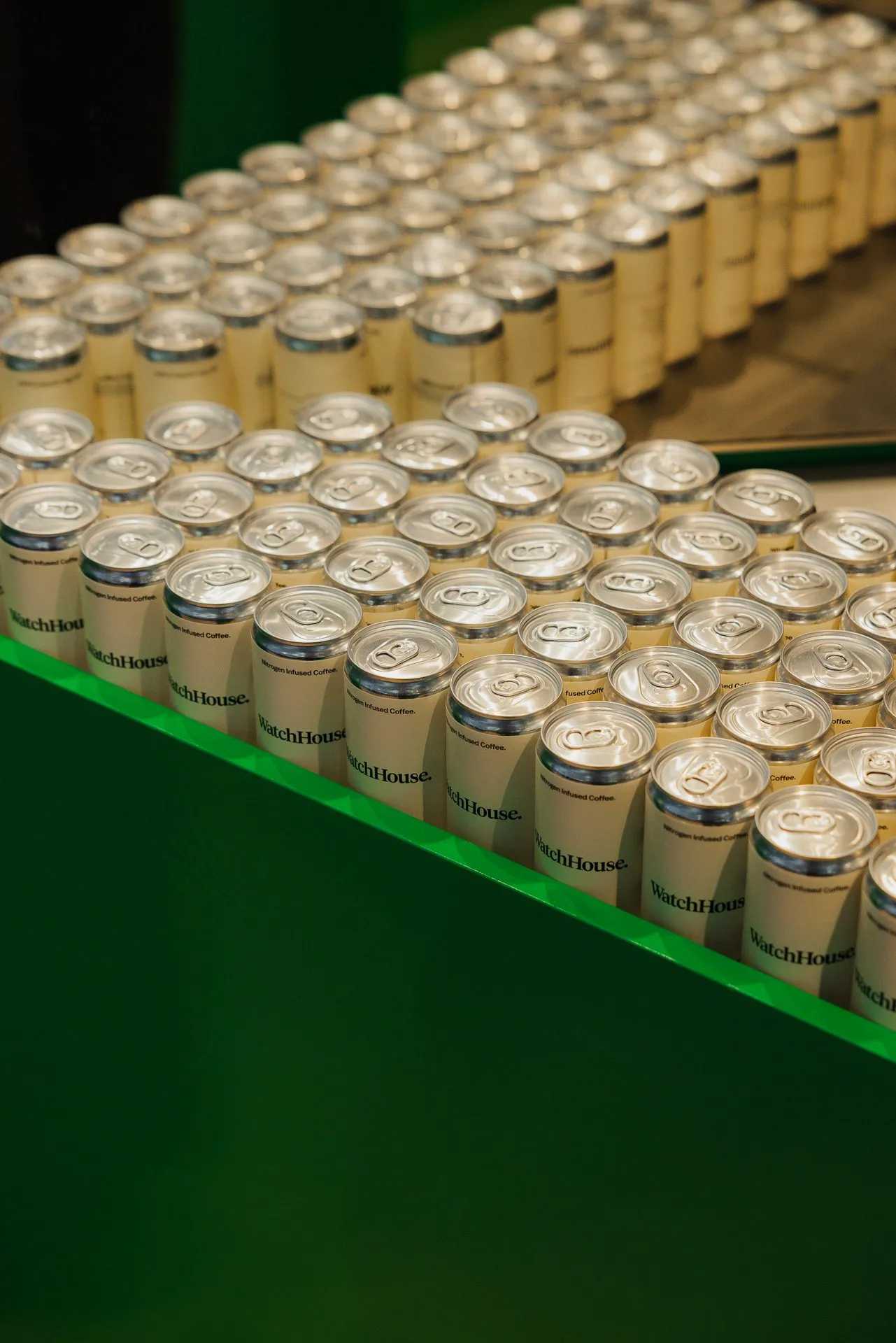 Rows of WatchHouse nitrogen-infused coffee cans on a green counter