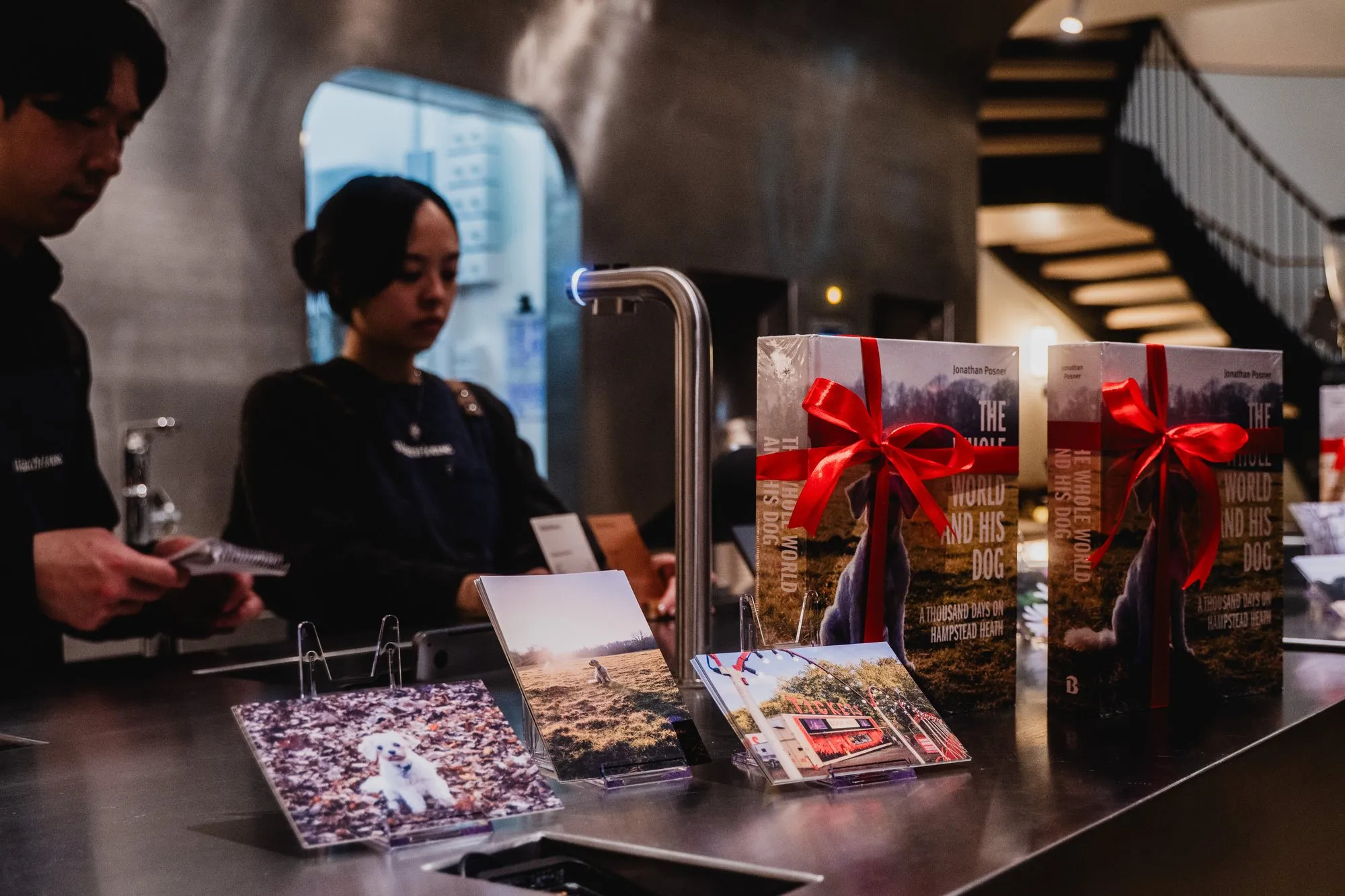 Copies of the book tied with red ribbon, next to postcards, at the launch